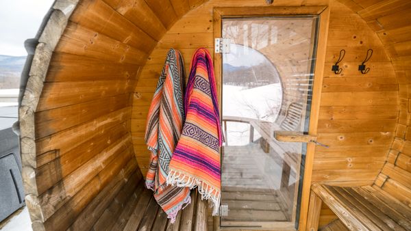 Inside view of a wooden sauna with colorful towels hanging, set against a snowy winter backdrop.