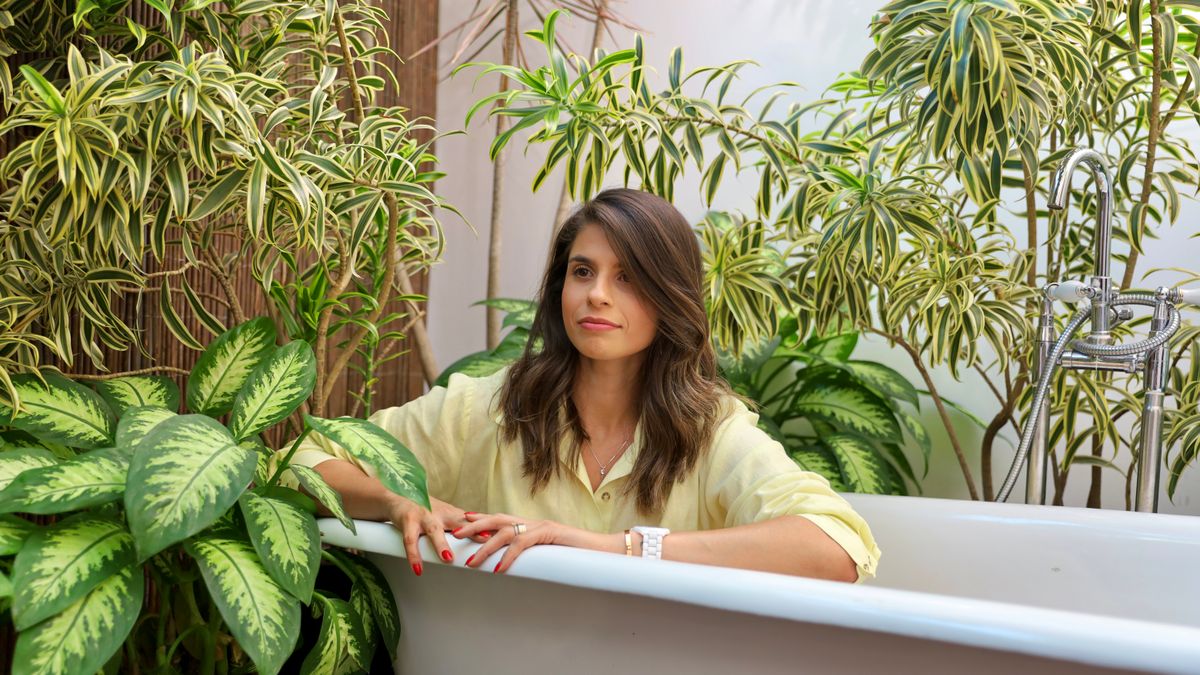 Flávia Vicentini / Pexels Woman enjoying a tranquil moment in an indoor garden bathtub surrounded by lush greenery.