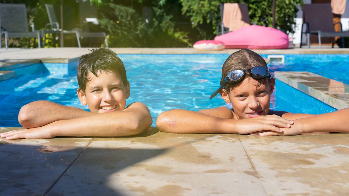Two kids smiling and relaxing in a swimming pool, enjoying a sunny vacation day.