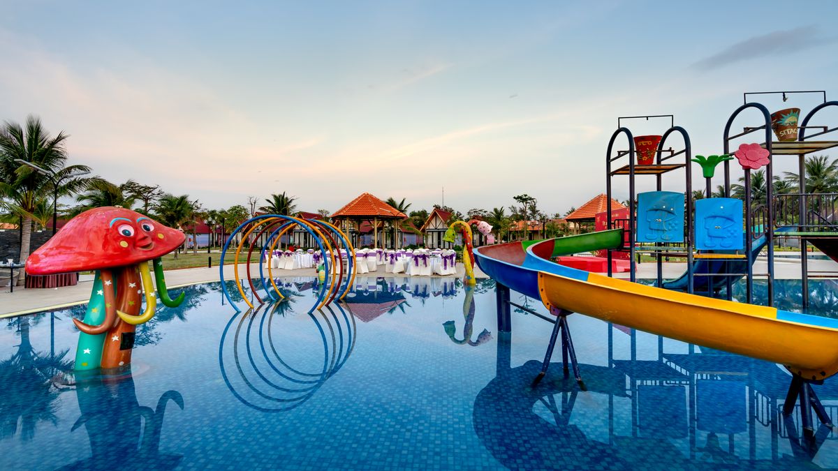 Quang Nguyen Vinh / Pexels Colorful waterpark with slides, mushroom-shaped feature, and palm trees reflecting in pool.