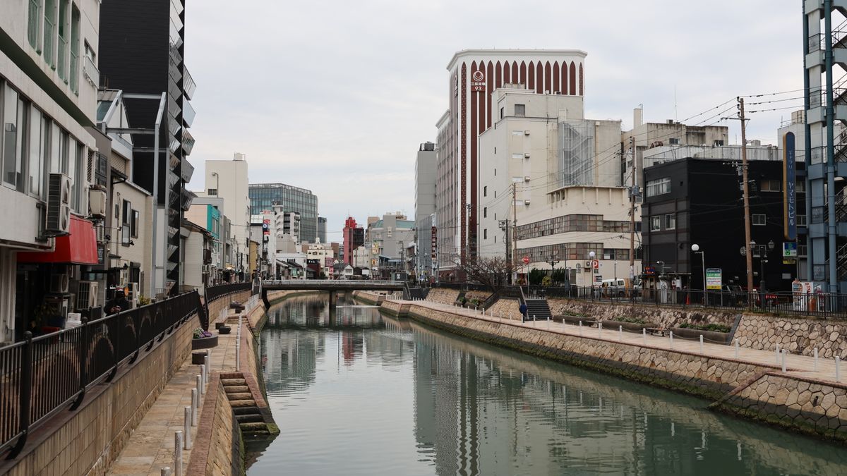 Serene view of a city canal in Fukuoka, Japan, flanked by modern architecture and reflective waters.