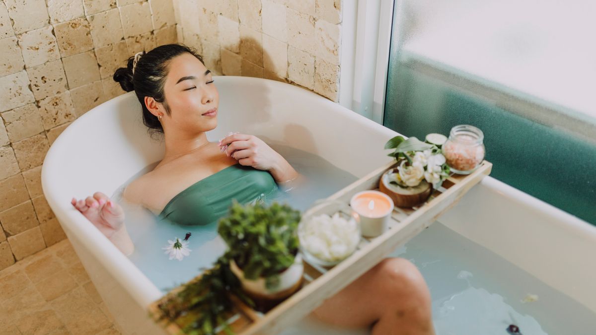 RDNE Stock project / Pexels Asian woman relaxing in a luxurious bathtub with a bath board and candles, enjoying a serene spa moment.