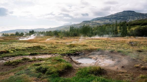 Scenic view of Icelandic hills and steaming hot springs under a cloudy sky.
