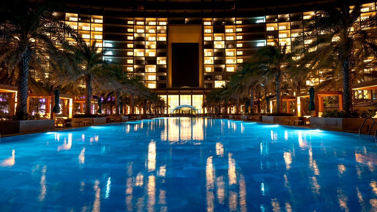Stunning night view of a hotel with palm-lined illuminated swimming pool reflecting lights.