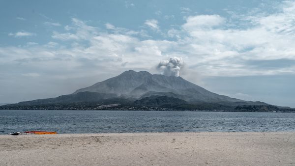Dramatic view of Sakurajima volcano erupting over a tranquil bay in Kagoshima, Japan.