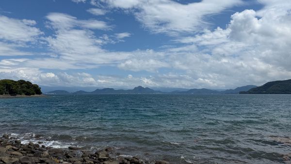 Beautiful coastal view of Kagoshima Bay with rocky shoreline, clear sky, and distant islands.