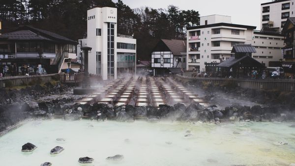 A tranquil hot spring town with steam rising from mineral-rich waters, surrounded by traditional architecture.