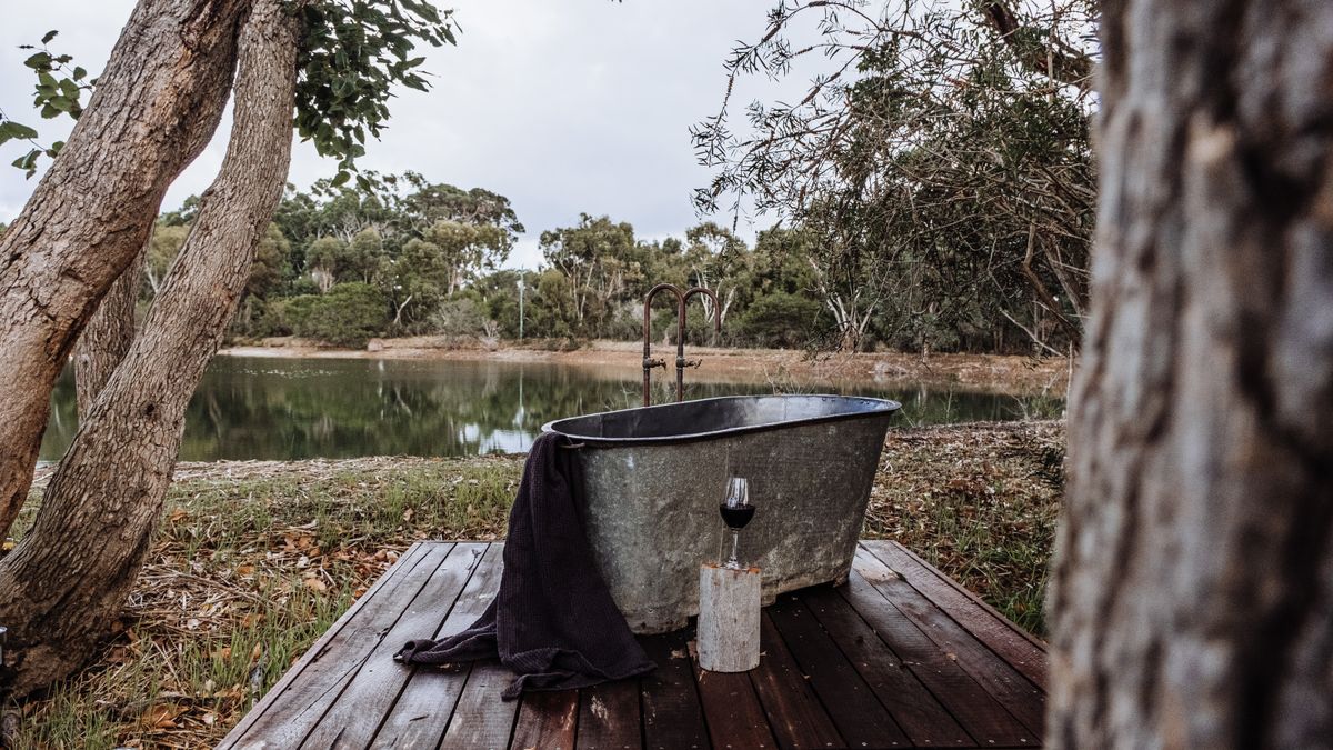 Rachel Claire / Pexels Relaxing rustic outdoor bathtub on a wooden terrace by a serene lakeside view.