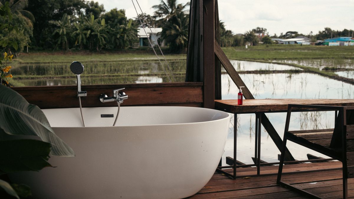 Relaxing outdoor bathtub on wooden deck overlooking a serene rural landscape.