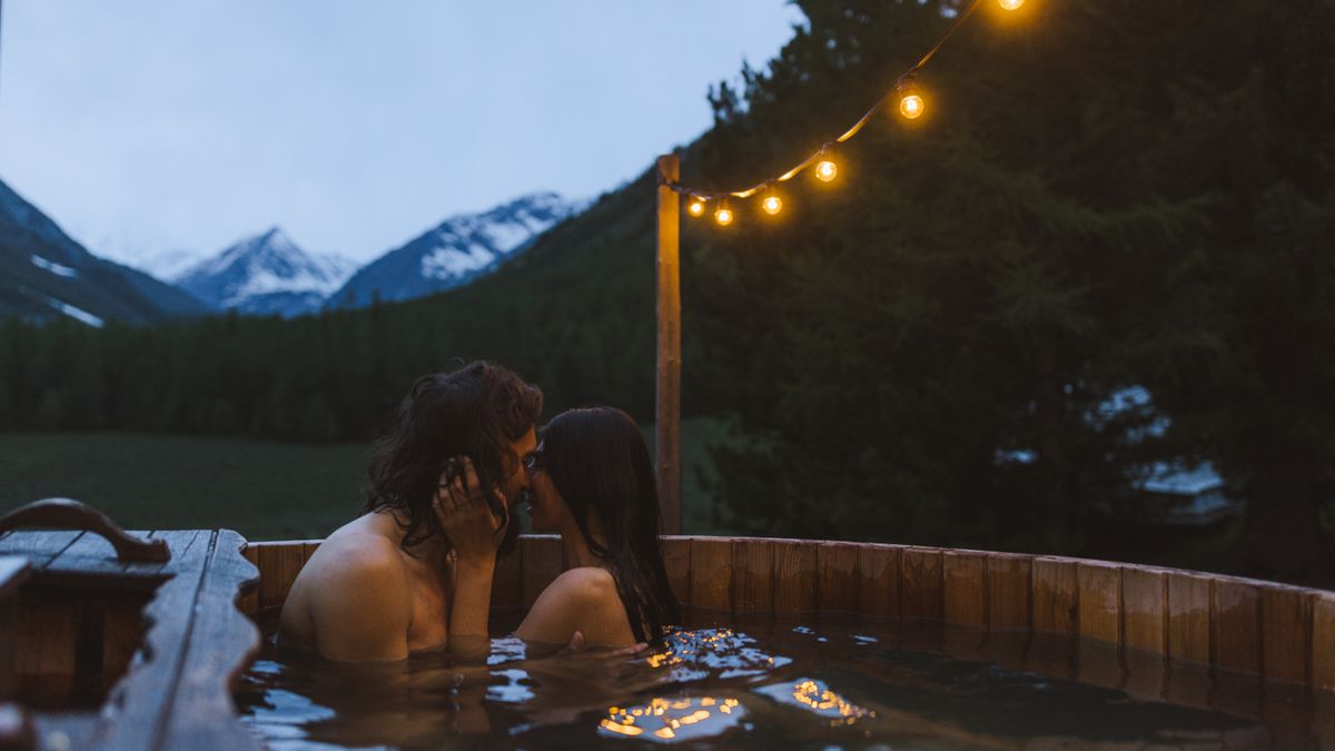 Yaroslav Shuraev / Pexels A couple shares a romantic kiss in a cozy outdoor hot tub surrounded by mountains at twilight.