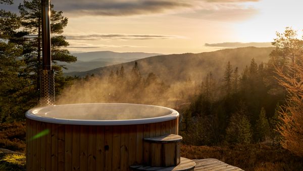 A steaming hot tub amidst the serene Norwegian countryside at sunset, offering stunning views.