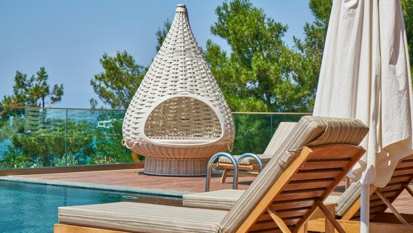 Elegant poolside setting featuring modern loungers and a unique woven chair in a tropical resort.