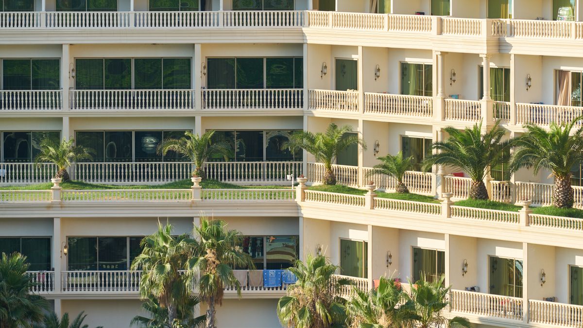 Elegant apartment building exterior with lush palm trees and balconies, ideal for vacation living.