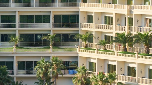 Elegant apartment building exterior with lush palm trees and balconies, ideal for vacation living.