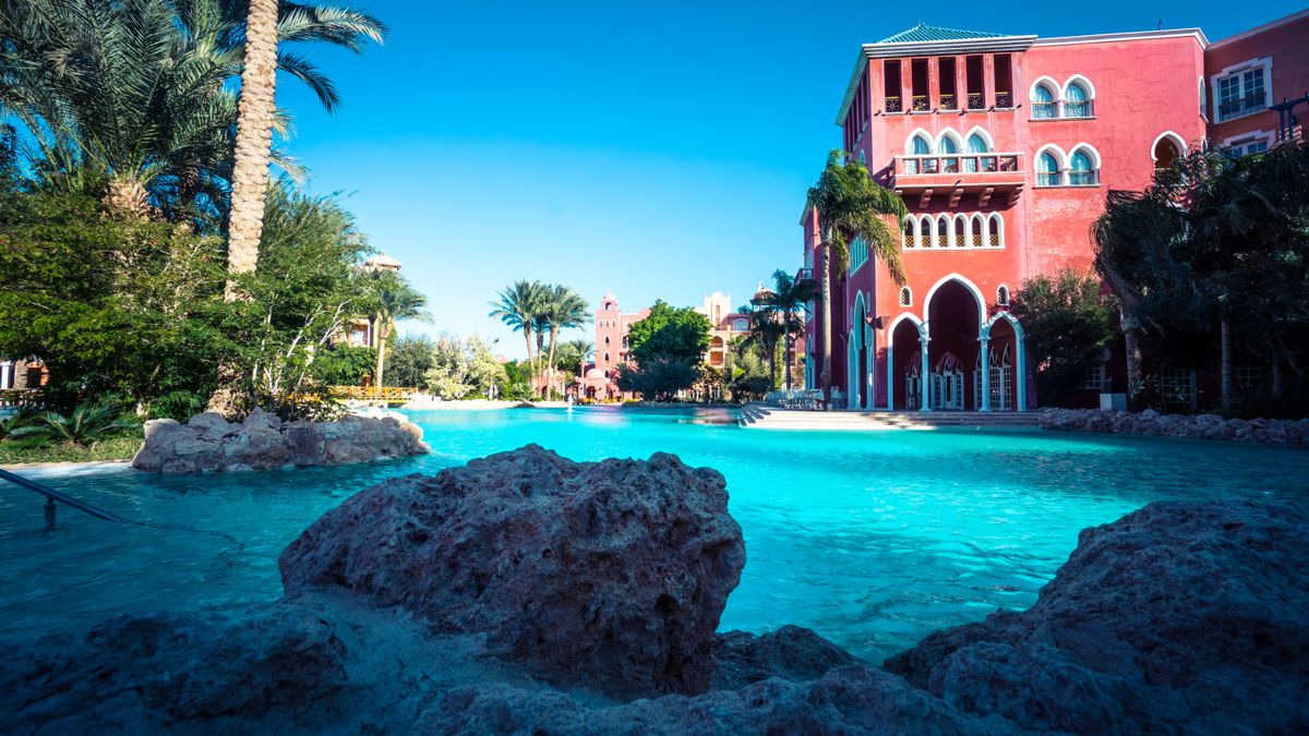Nikolaj Erema / Pexels Stunning resort poolside area with palm trees and vibrant red architecture on a sunny day.