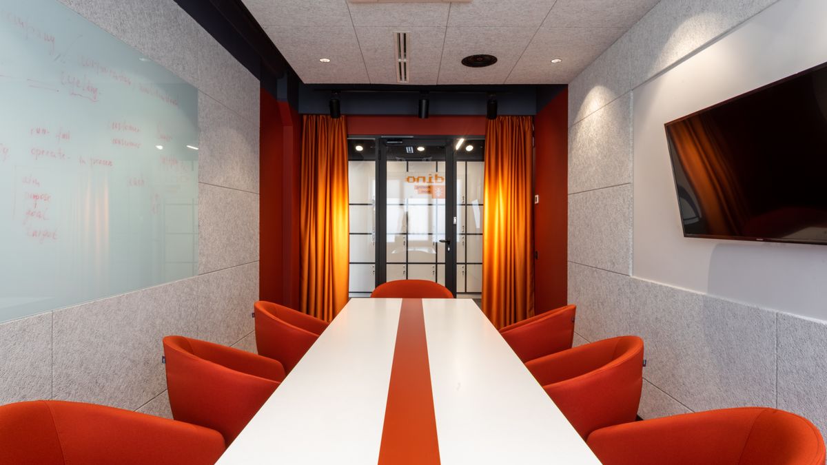 Set of comfortable orange armchairs placed around long white table in modern workspace with TV on wall and glass door