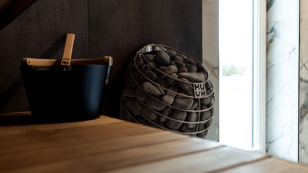 HUUM │sauna heaters / Pexels A sleek and modern indoor sauna featuring an elegant stone heater and wooden bucket, perfect for relaxation.