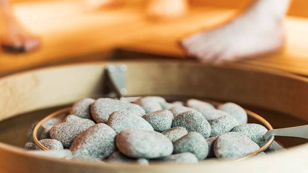 Close-up of sauna stones with blurred feet in a warm, indoor sauna setting.