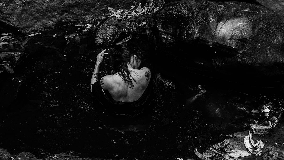 A woman soaking in a natural rock pool, captured in a moody black and white scene.