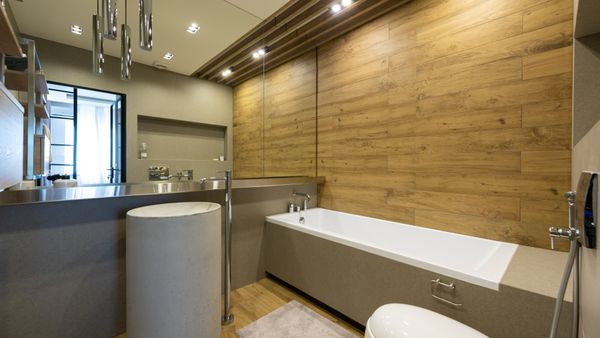Contemporary design of bathroom with stylish lamps shining above sink bath and toilet